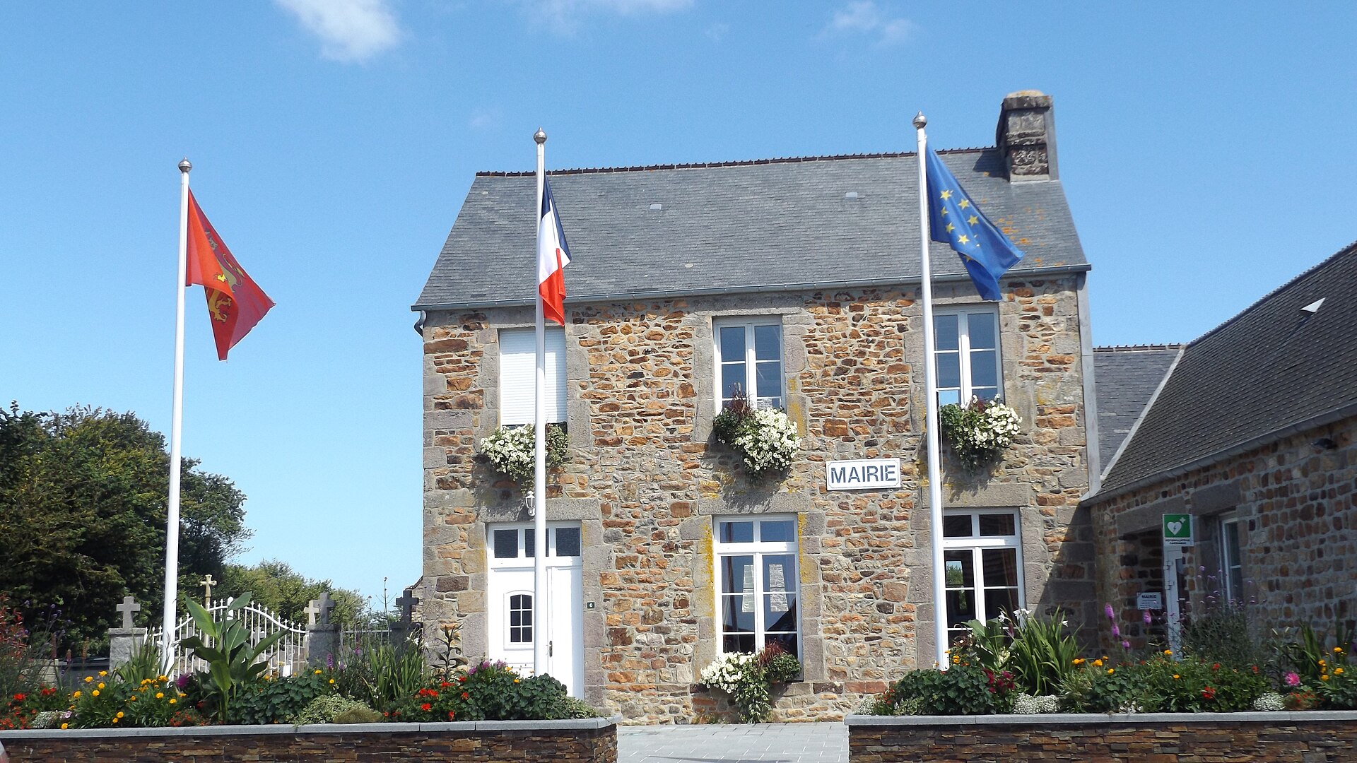 Façade en pierre de la mairie de Vasteville, avec les drapeaux normand, français et européen